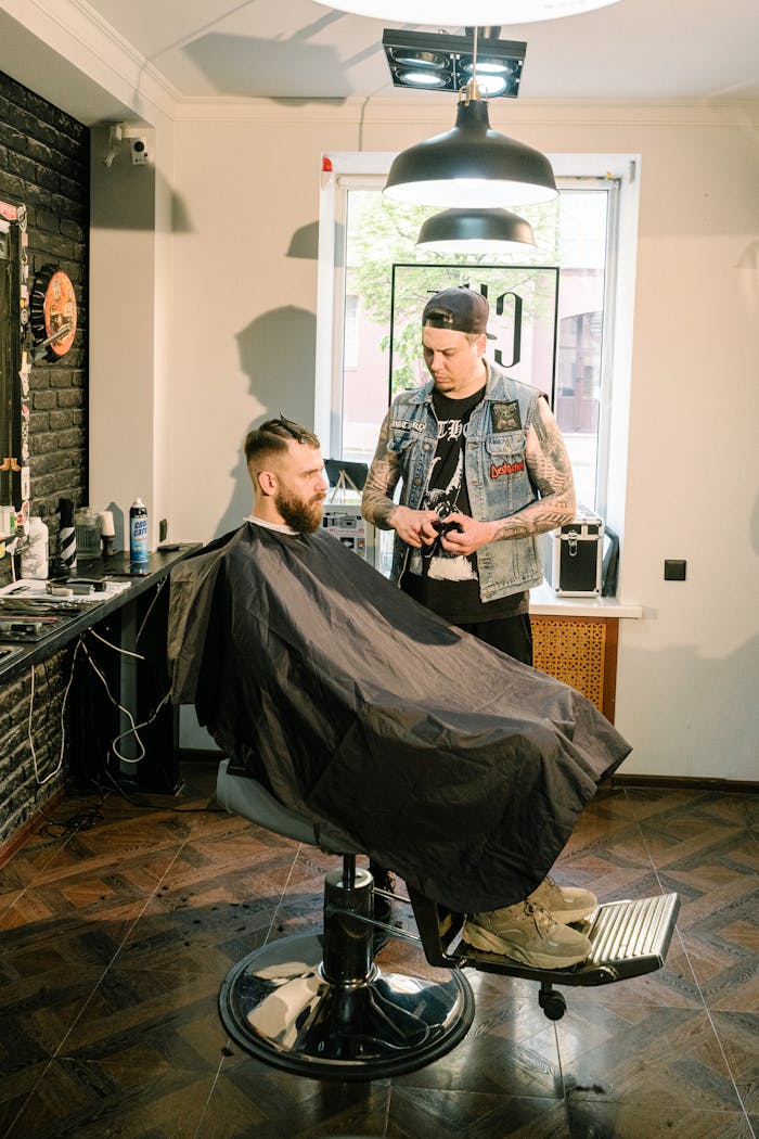 A tattooed barber styling a client's hair in a trendy salon setting.